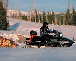 Мужчина едет на снегоходе с груженым прицепом